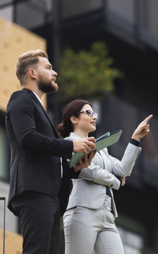 A man and woman are standing outside with papers in their hands.