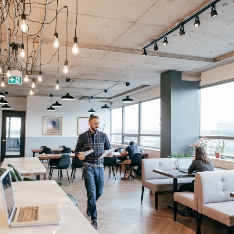 A man walking through an office with people sitting at tables.