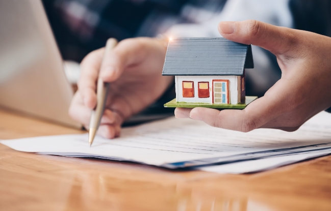 A person holding a pencil and house model